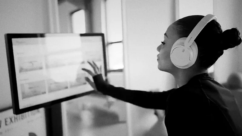 Cliente avec un casque choisissant sa séance sur le kiosque tactile d'un studio de Pilates Reformer digital, en noir et blanc