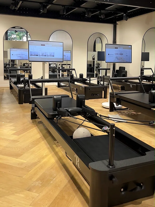 Studio client équipé par Reformer Society : Reformers alignés, un écran sur pied devant chaque machine